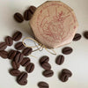 A brown coffee bean stamp mold is shown with loose coffee beans scattered around it.