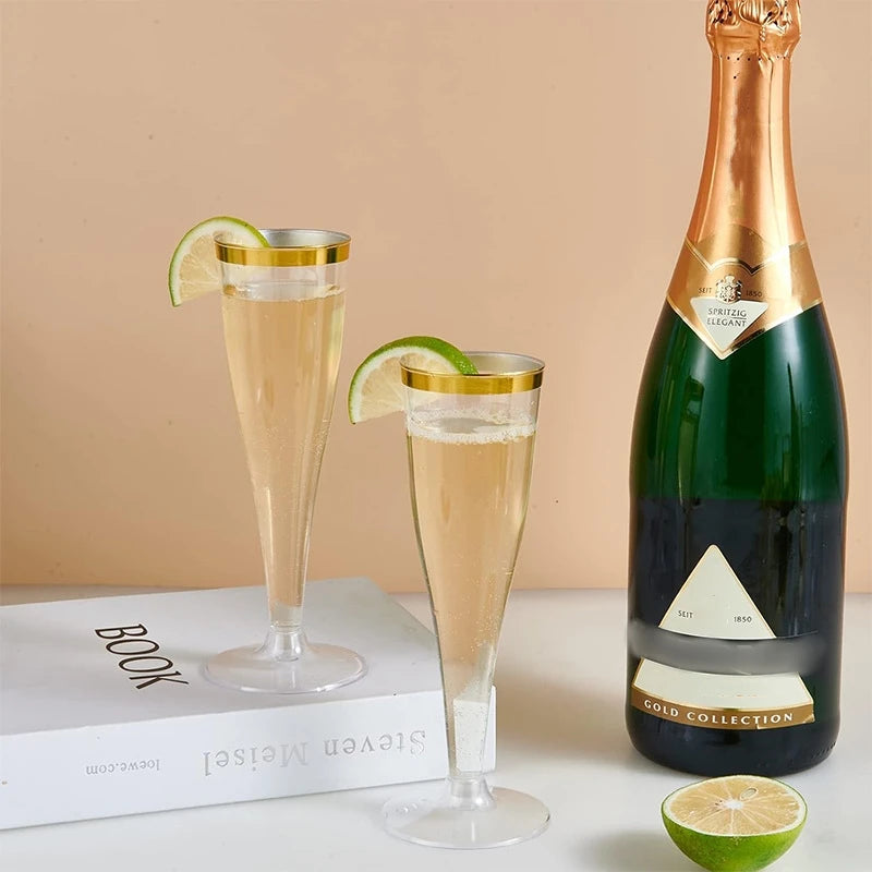 A bottle of sparkling wine next to clear plastic champagne flutes and a lime slice.