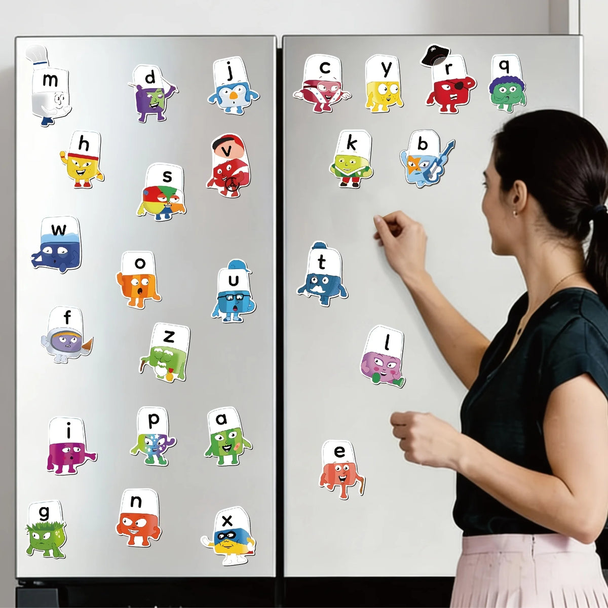 A woman is using 26-piece popsicle alphabet magnets to write letters on a white surface.