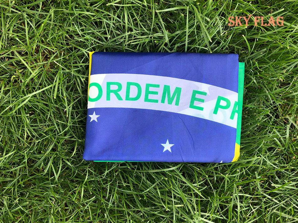 A folded blue flag with green text reading ORDEM E PA displayed on green grass.