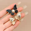 A hand holds a black butterfly-shaped clip with a pearl and a gold butterfly clip.