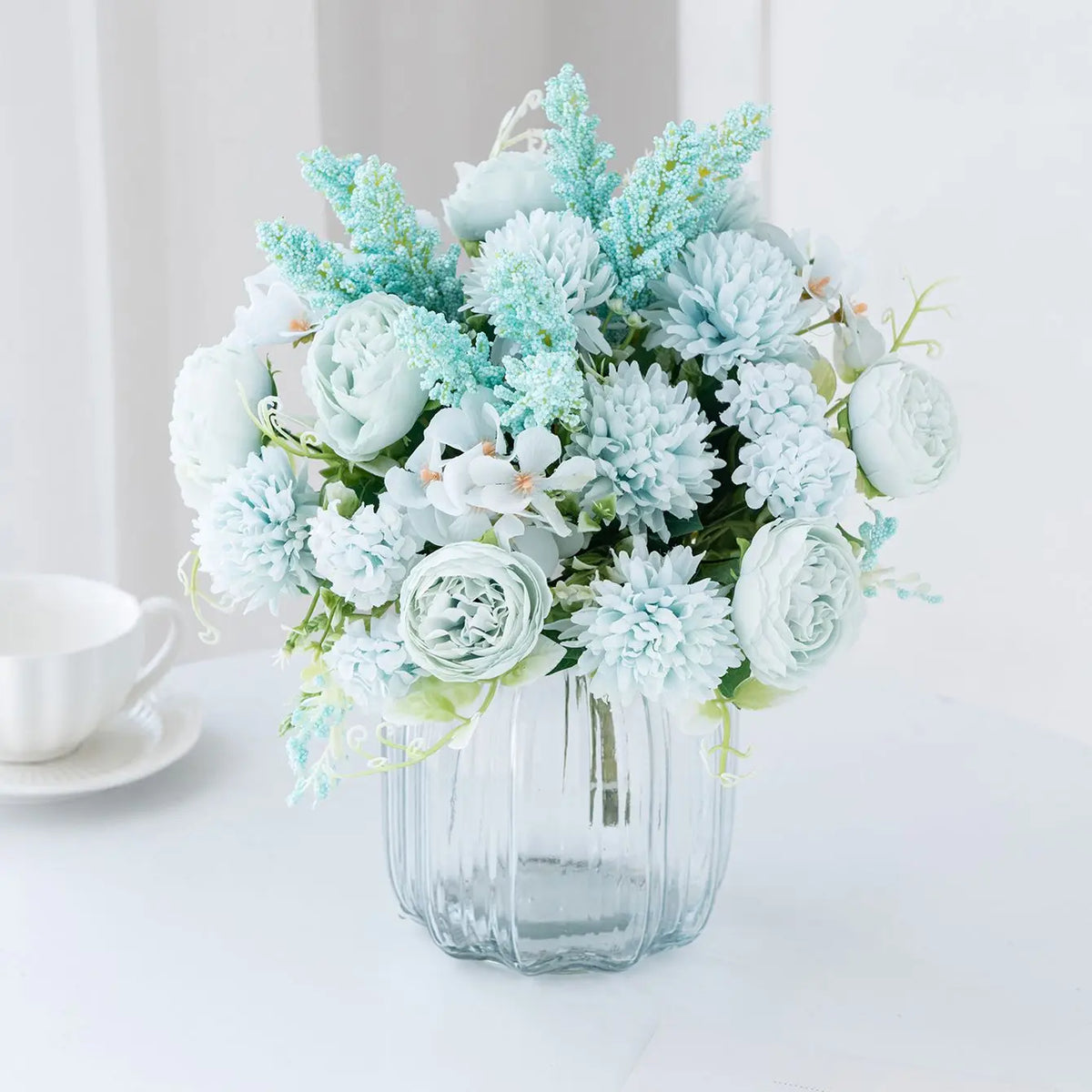 A bouquet of light blue and white artificial silk peony flowers arranged in a clear glass vase.