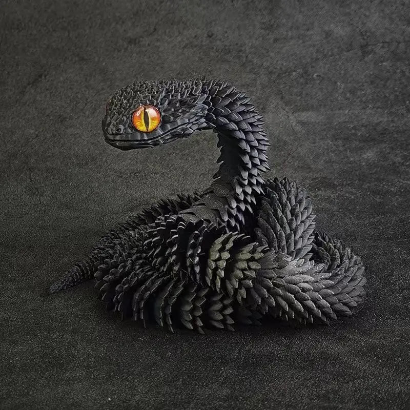A dark, textured 3D printed snake art model with an amber eye, resting on a dark gray surface.