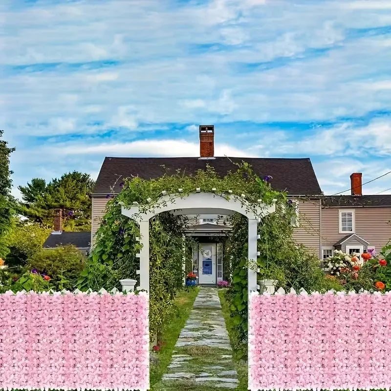 A white arched entryway covered in green vines leads to a house, framed by pink artificial cherry blossom privacy fences.