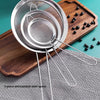 A set of three stainless steel colanders and strainers resting on a wooden board and gray fabric.