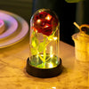 Ein Glasgefäß mit einer roten Rose und leuchtenden LED-Lichtern auf einer Marmoroberfläche.