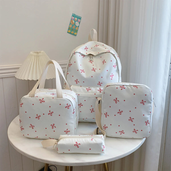 A set of white backpacks and accessories featuring a red bow print on a light-colored surface.