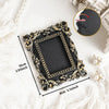 A black vintage baroque resin hanging photo frame with gold accents displayed on a white fluffy surface.