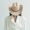 A woman wearing a beige wool cowboy hat with a studded leather band and a white collared shirt.