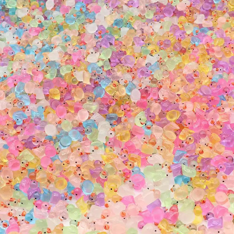 A close-up of numerous glow-in-the-dark Christmas duck figurines with Santa hats scattered across a light background.