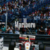 A vintage Formula 1 car is visible on the track with a large crowd in the background.