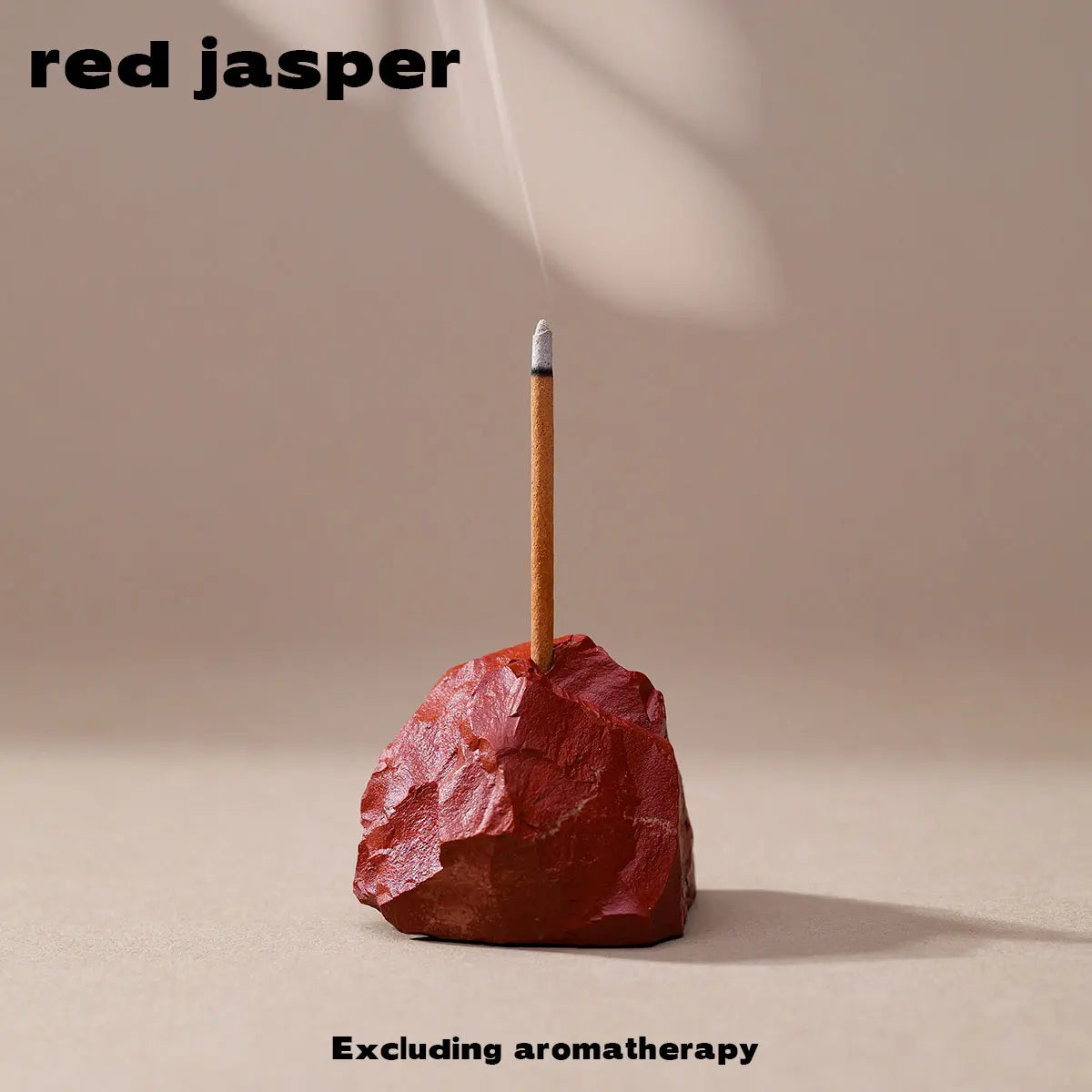 A stick of red jasper is shown resting on a reddish-brown rock, with smoke rising above it.