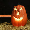 Linterna de calabaza de cerámica naranja tallada con ojos y dientes amarillos brillantes, sobre paja.