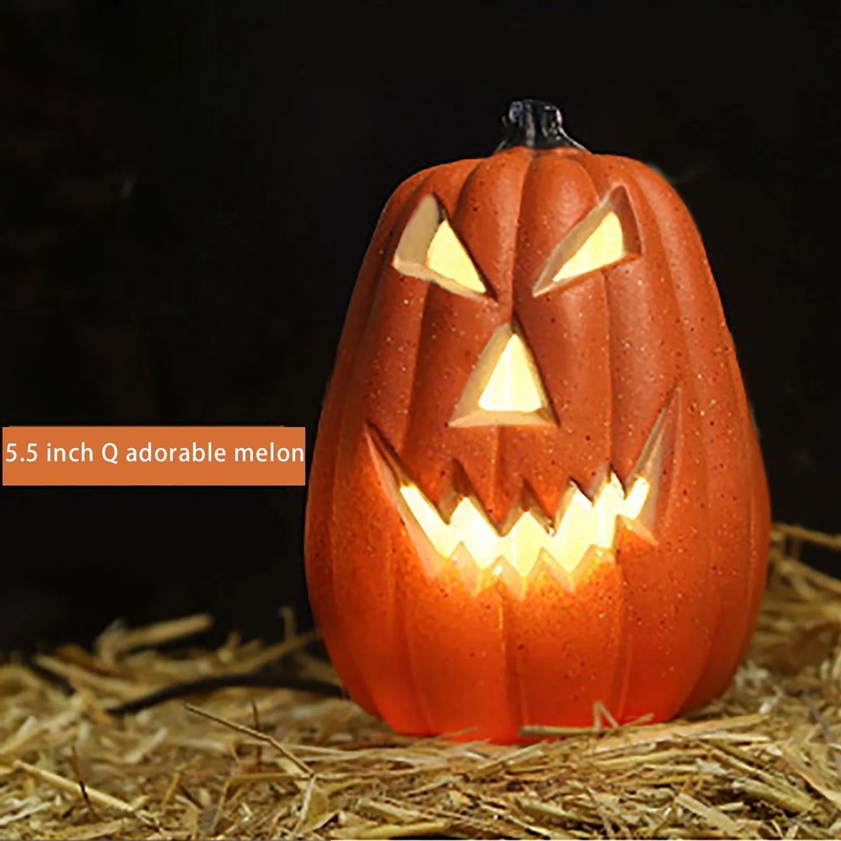 Linterna de calabaza de cerámica naranja tallada con ojos y dientes amarillos brillantes, sobre paja.