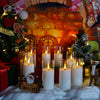 A festive holiday display featuring five glass candles on a white surface in front of a brick fireplace background.