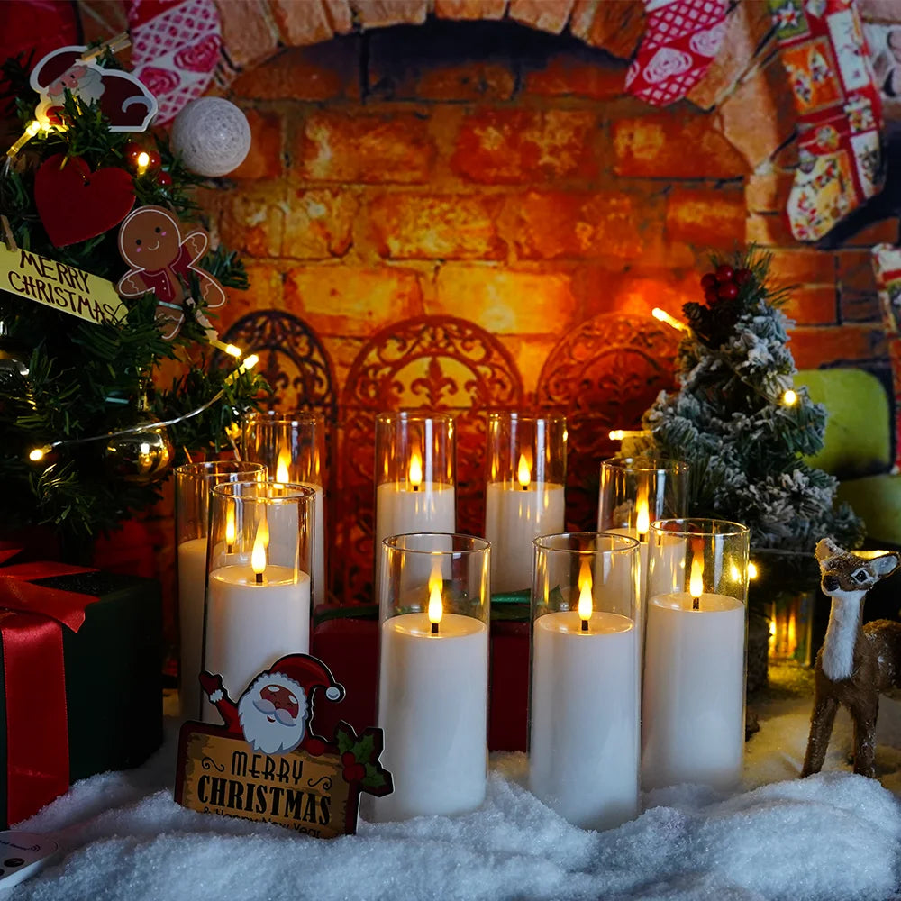 A festive holiday display featuring five glass candles on a white surface in front of a brick fireplace background.