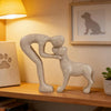 A light gray sculpture depicting a human and a dog embracing, displayed on a wooden shelf.