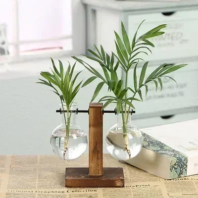 A vintage hydroponic plant vase with green leaves sits on a wooden stand.