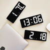 A black LED digital alarm clock displaying time, temperature, and other functions, resting on a white laptop.