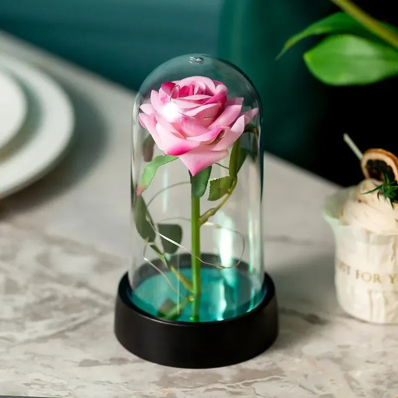 Glaskuppel mit rosa Rose und grünem Stiel, beleuchtet durch LED auf schwarzem Sockel