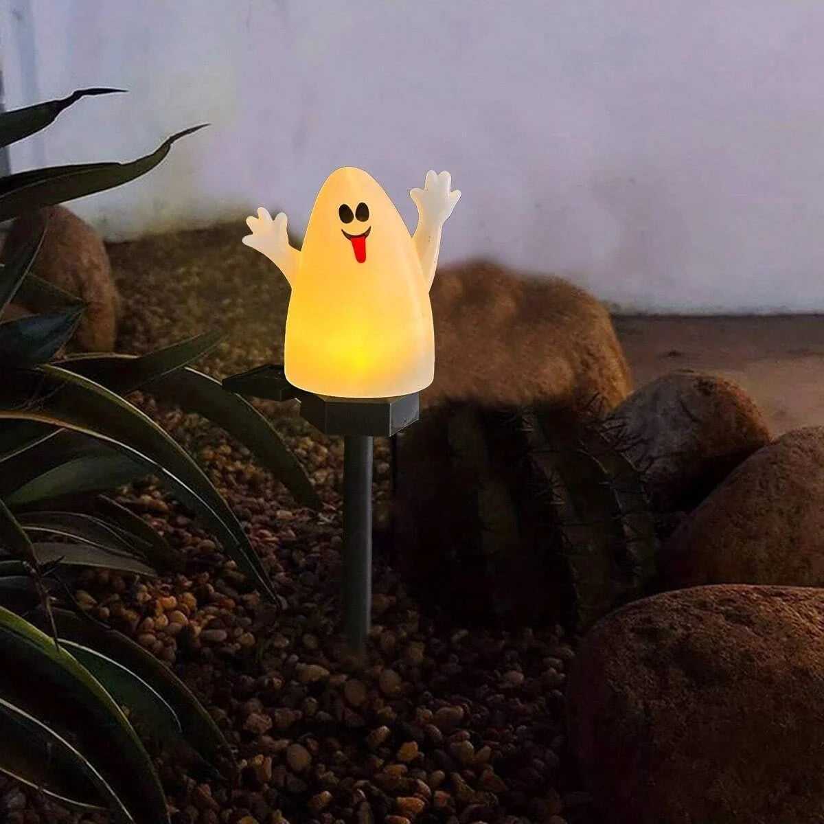 Une guirlande de Halloween jaune et lumineuse en forme de fantôme souriant est placée dans la terre sombre du jardin parmi le