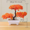 An artificial tree bonsai decoration with bright orange foliage planted in a white rectangular pot.