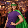 A woman wearing a purple shirt and green cape with a green eye mask, posing in a costume setting.