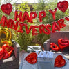 Red foil balloons spelling HAPPY ANNIVERSARY hanging outdoors among green foliage