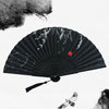 A black vintage bamboo folding hand fan with delicate white leaf designs against a white background.