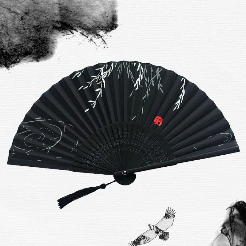 A black vintage bamboo folding hand fan with delicate white leaf designs against a white background.