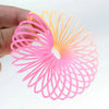 A hand holds a bright pink and orange rainbow magic spring toy with numerous thin, curved wires forming a flower shape.