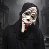 A white, stylized mask resembling a face with a protruding red tongue is worn by a figure in a black cloak amidst a foggy, da