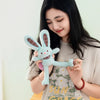 A woman holds a light blue giant kawaii rabbit plush toy against a pale green background.