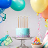 A tiered cake decorated with colorful sprinkles and topped with numerous birthday candles, surrounded by balloons.