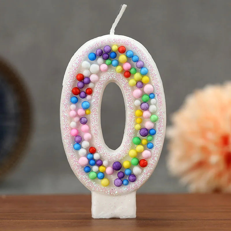 A white candle shaped like the number zero decorated with colorful candy beads for a birthday celebration.