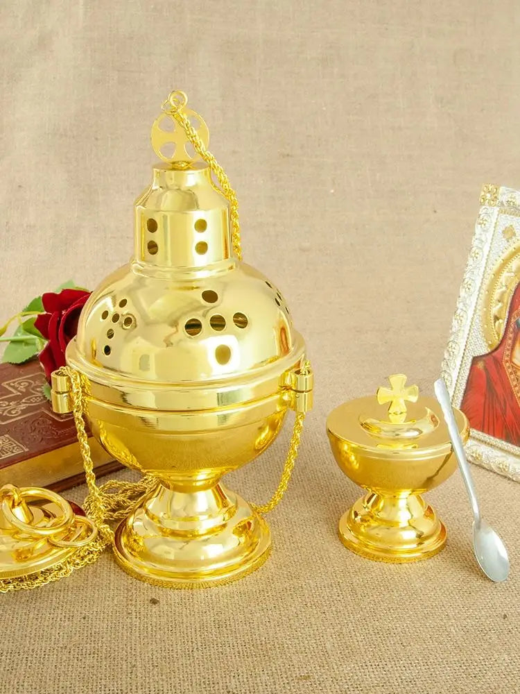 A gold-plated Orthodox censer with bells hanging by a chain, set against a beige background.