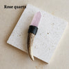 A rose quartz crystal point mounted on a dark wood wand with black cord for spiritual decor.