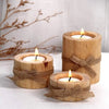 A set of rustic wooden stump candle holders tied with twine, displayed on a white surface next to dry branches.