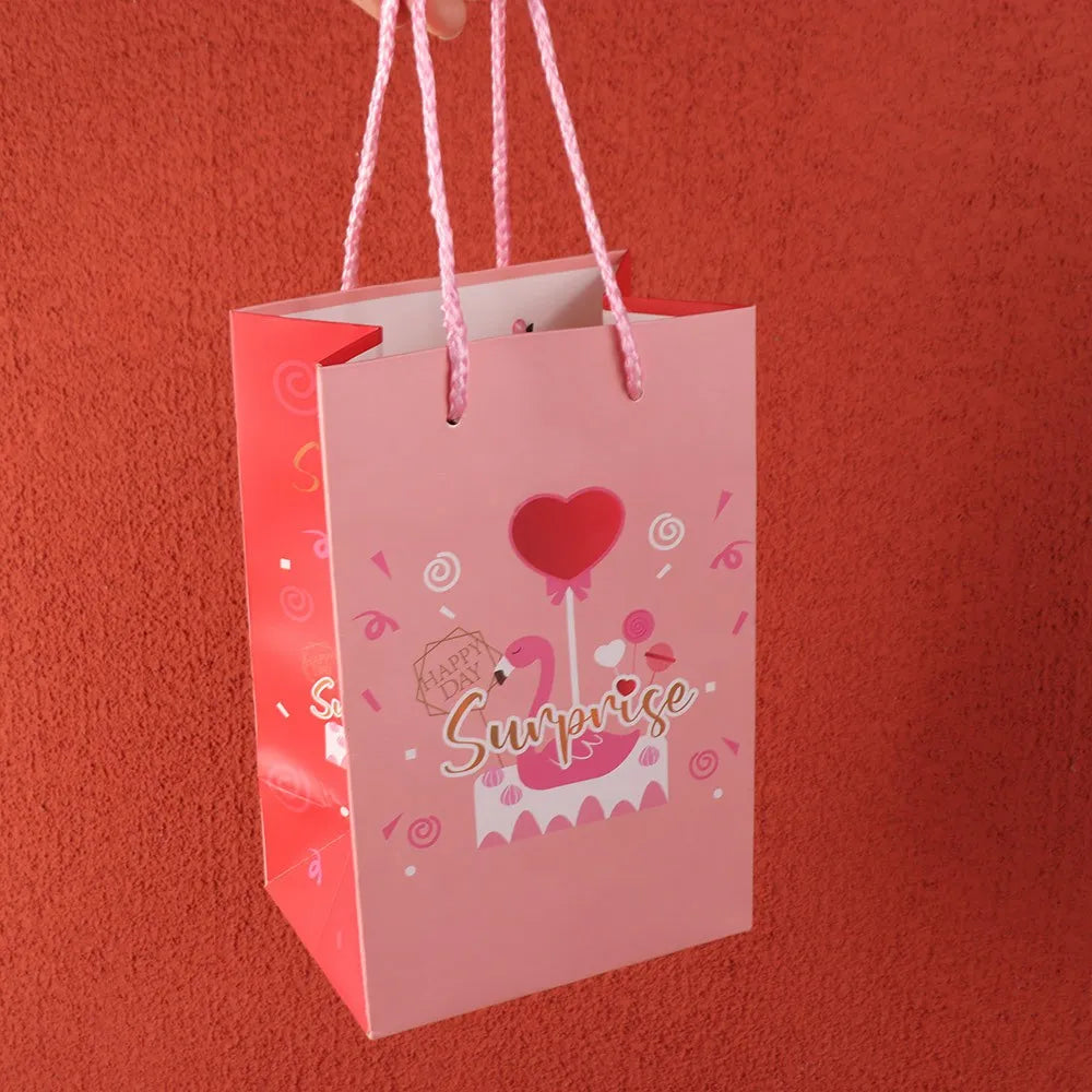 A pink paper gift bag with pink ribbon handles and a heart-shaped pink balloon, featuring the word Surprise.
