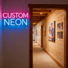 A custom neon sign spelling CUSTOM NEON is displayed on a white wall next to a wooden doorway.