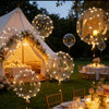 Golden LED illuminated party balloons floating above a rustic outdoor wedding reception.