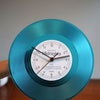 A teal vintage vinyl record wall clock showing the time, with a transparent cover and wooden base.