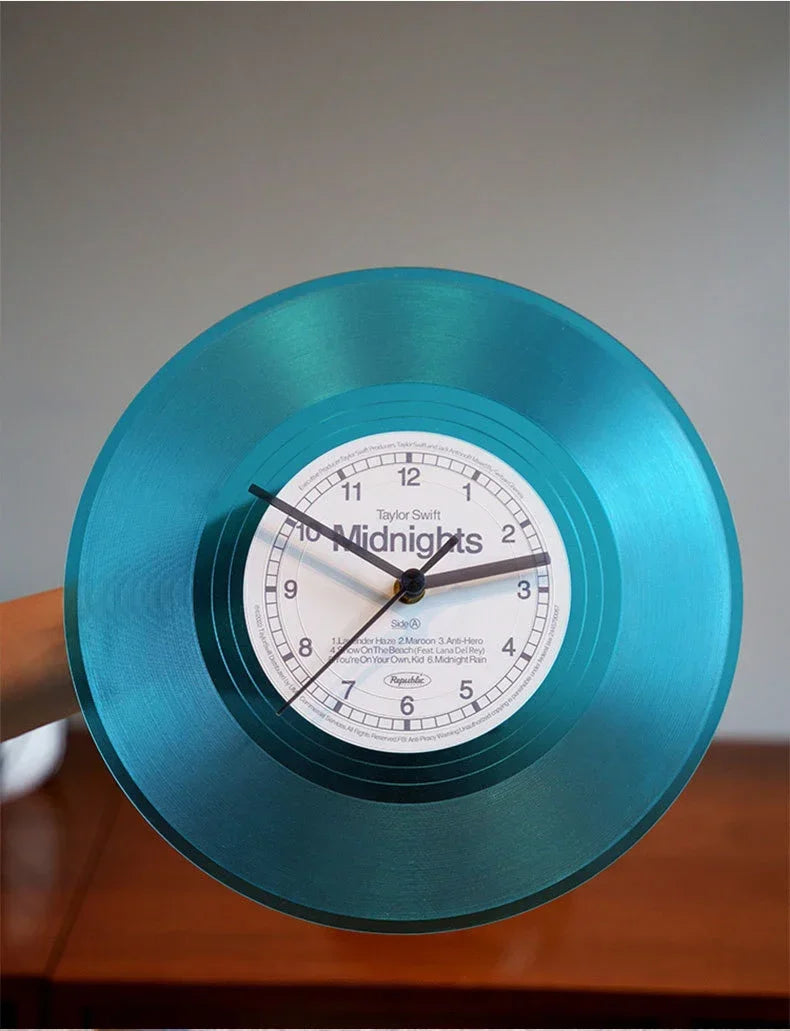 A teal vintage vinyl record wall clock showing the time, with a transparent cover and wooden base.