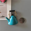 A teal teapot shaped fridge magnet with a black handle and gold accents.