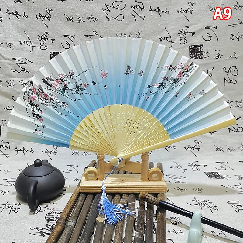 Elegant vintage Chinese folding hand fan with light blue and yellow blades displayed on a wooden stand.