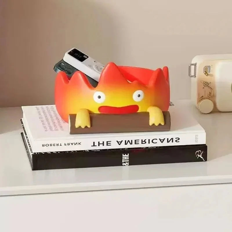 A resin cartoon fire person tray with an orange head and yellow horns rests on a stack of books.