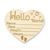A heart-shaped natural wood baby milestone disc with 'Hello World' text and lines for recording baby details.