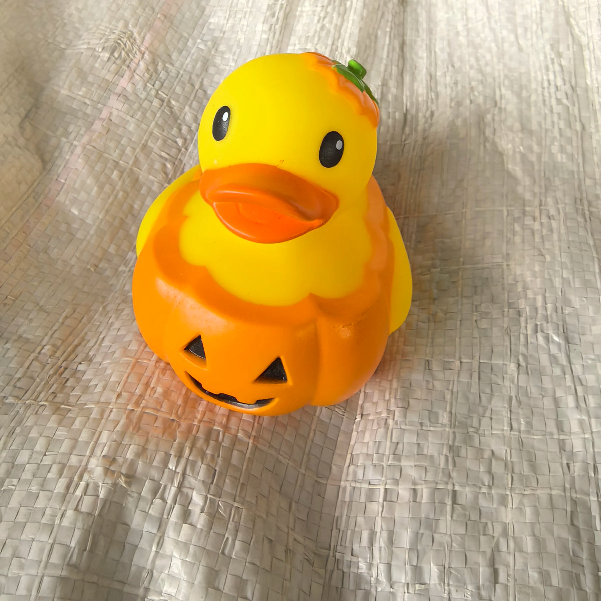 A bright yellow rubber duck bath toy with an orange belly and a green top, resting on wrinkled light-colored fabric.