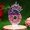 Glitter number 6 birthday candle with a rhinestone crown cake topper displayed on a wooden slice.