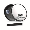 A black magnifying compact mirror with a circular lens and a suction cup is shown on a white background.